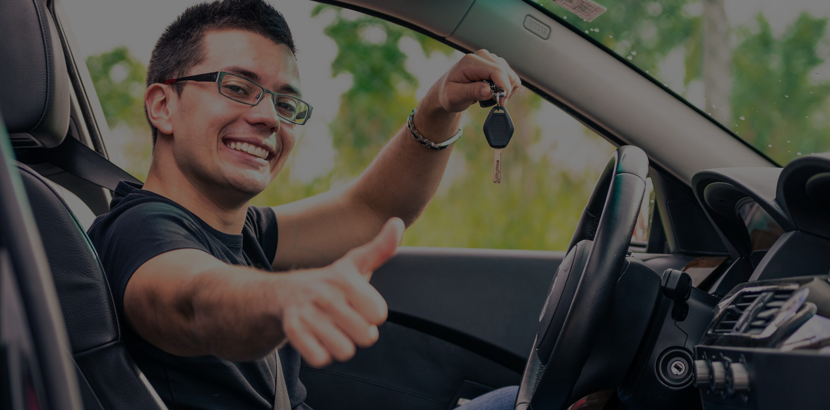 A man smiling and giving a thumbs-up while holding car keys inside a car.